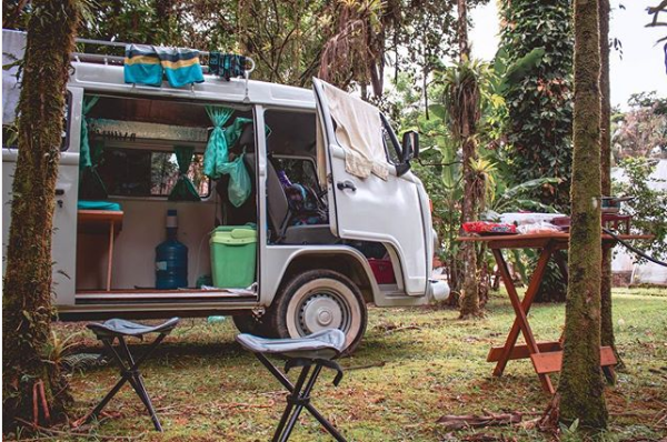 Imagem de um Kombi com a porta aberta, com vários equipamentos e coisas para fora.