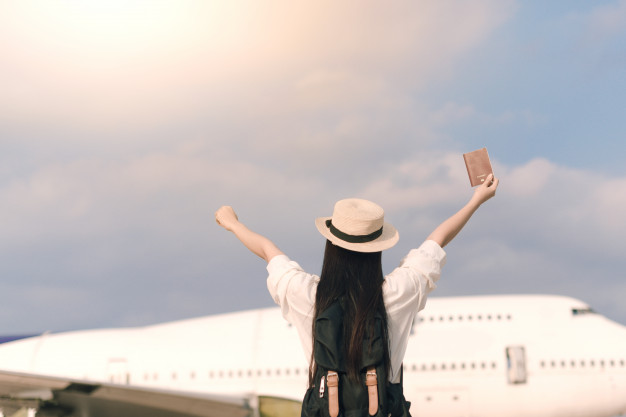 Menina ao lado do avião com os braços para cima