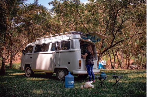 Kombi estacionada, com uma menina cozinhando na parte de trás