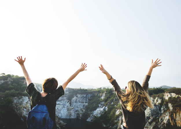 Duas mulheres viajantes e nômades digitais com os braços para cima.